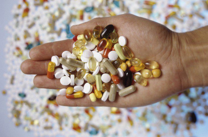 Person's hand holding an assortment of tablets and capsules
